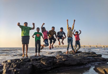 boy-wearing-green-crew-neck-shirt-jumping-from-black-stone-on-seashore