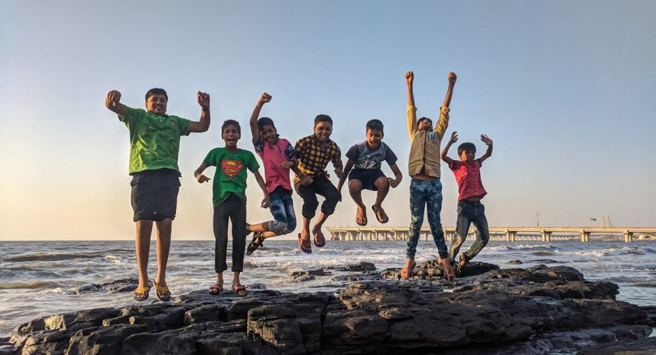 boy-wearing-green-crew-neck-shirt-jumping-from-black-stone-on-seashore