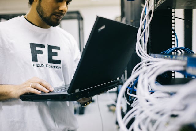 serious-ethnic-field-engineer-examining-hardware-and-working-on-laptop