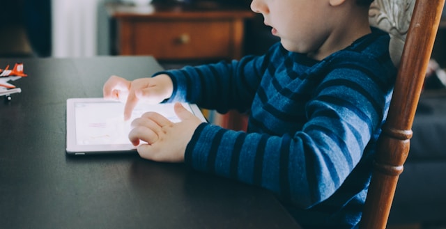 boy-sitting-on-chair-beside-table-using-tablet-computer