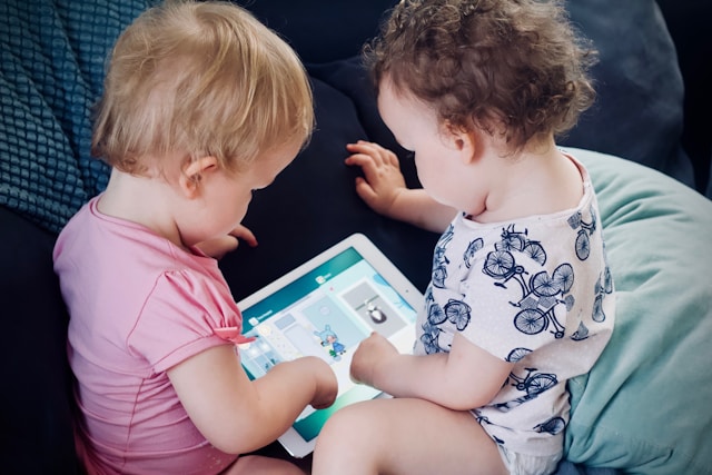 two-toddlers-sitting-on-sofa-while-using-tablet-computer